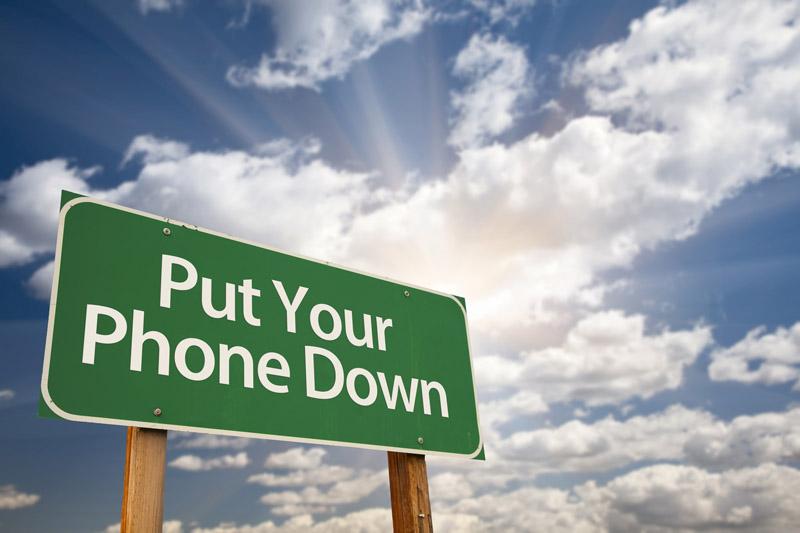 Put Your Phone Down Green Road Sign with Dramatic Sky, Clouds and Sun.